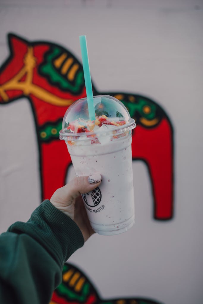 Vivid milkshake with whipped cream and straw held against folk art background.